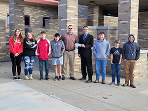 PARSS representative handing a check to a teacher next to students outside building